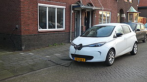 EV-kabelgoottegel Op de afbeelding is een auto te zien die staat geparkeerd in de openbare ruimte. De kabel ligt door de kabelgoottegel niet op het troitter, maar in de tegel.